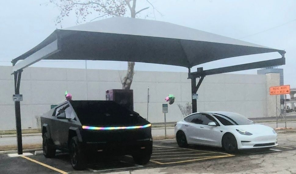 Two parked cars under a large canopy in a foggy outdoor lot, one black and one white.