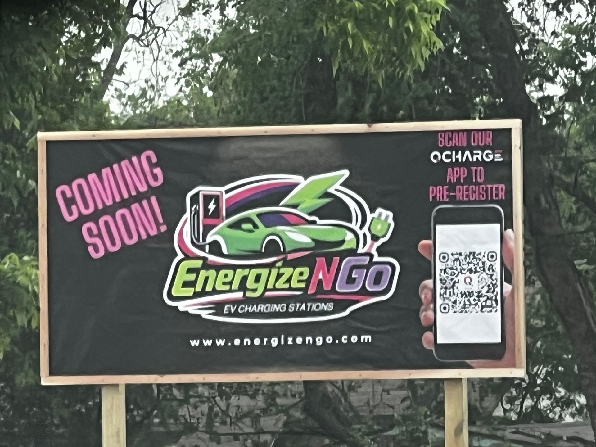 EnergizeNGo charging station billboard with “Coming Soon” text, QR code, and sign-up prompt on black background
