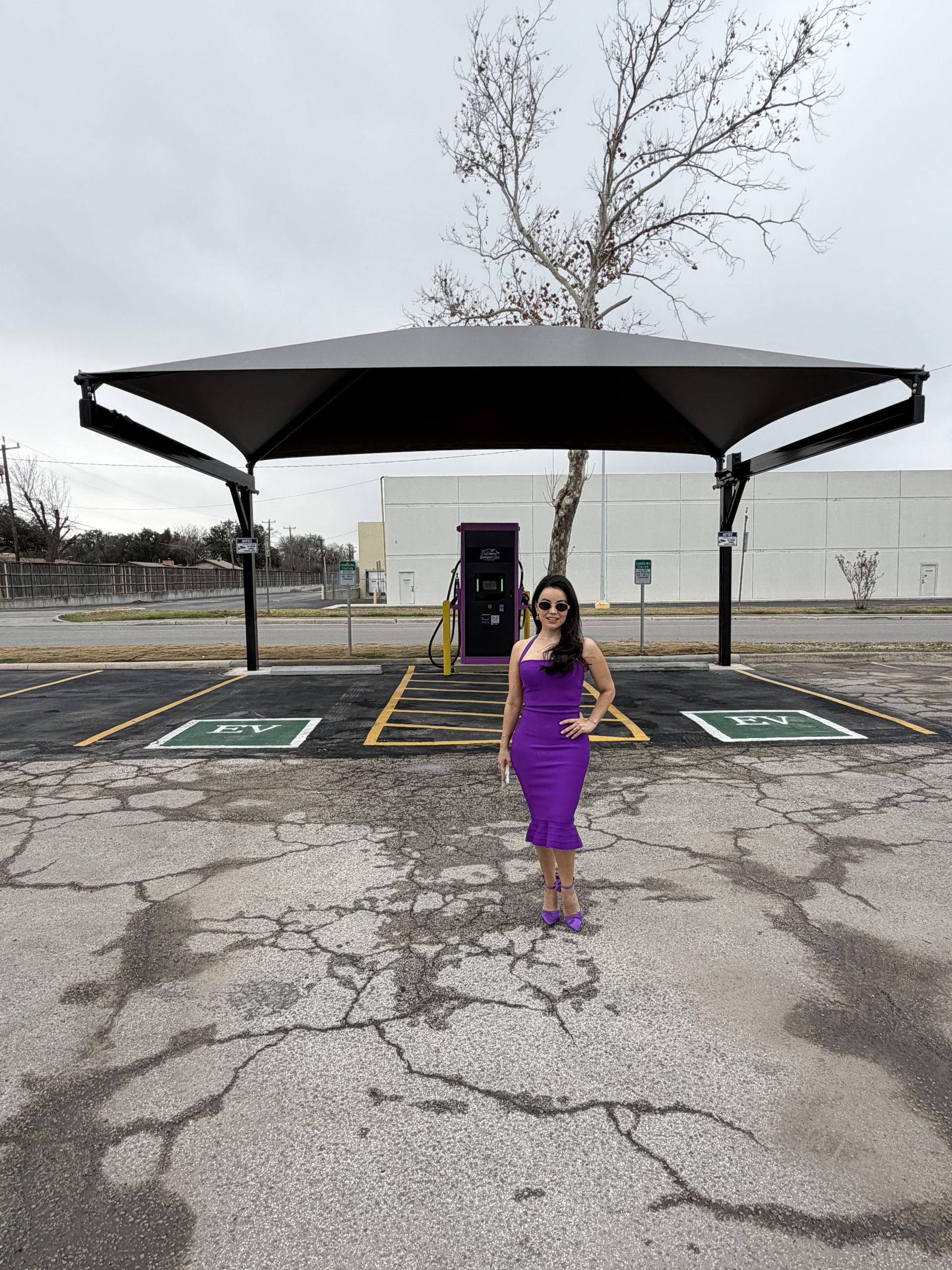 Woman in purple dress standing in an empty parking lot under a black canopy.