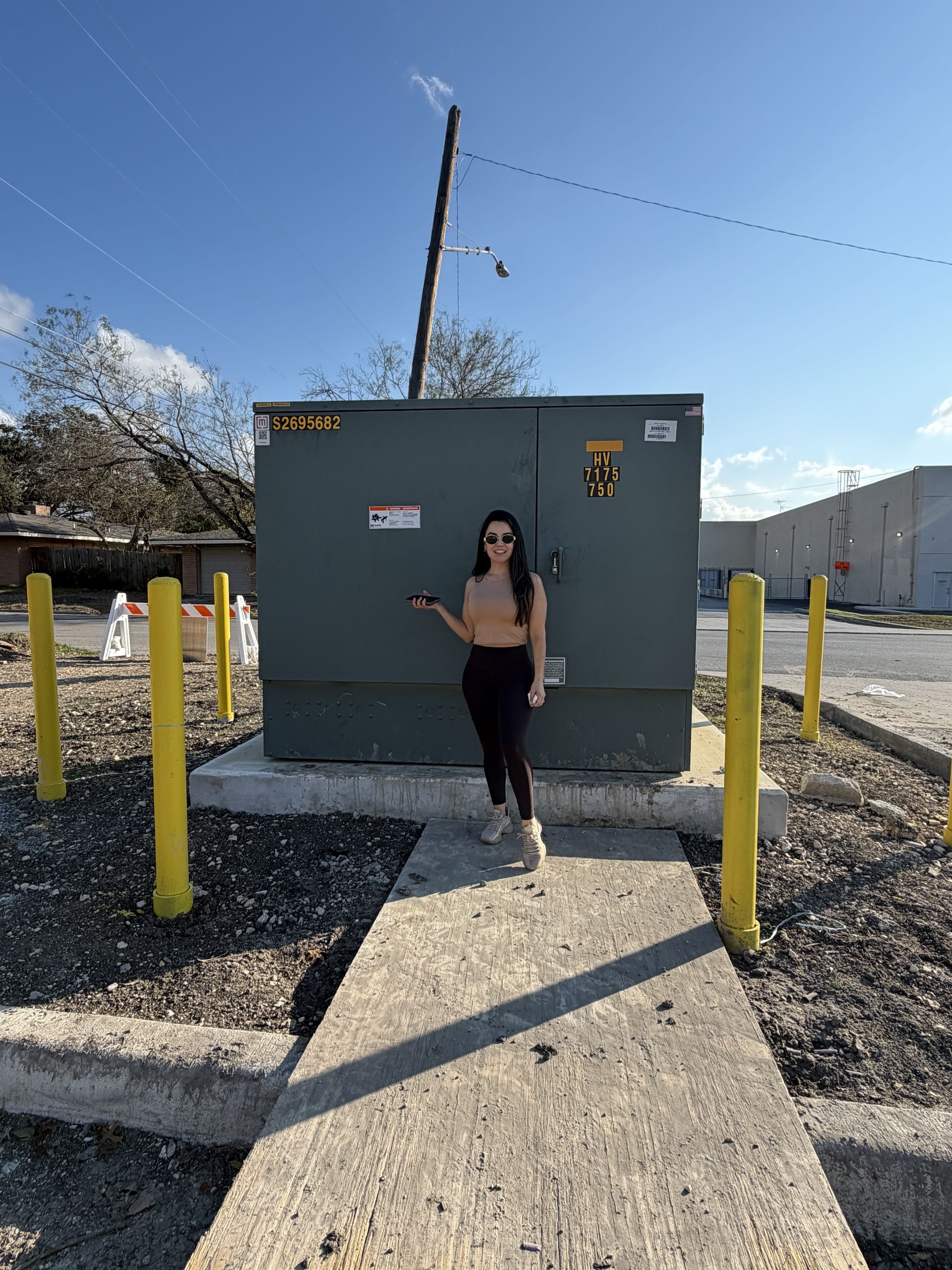 Person standing in front of a gray utility box with yellow posts and mountains in the background