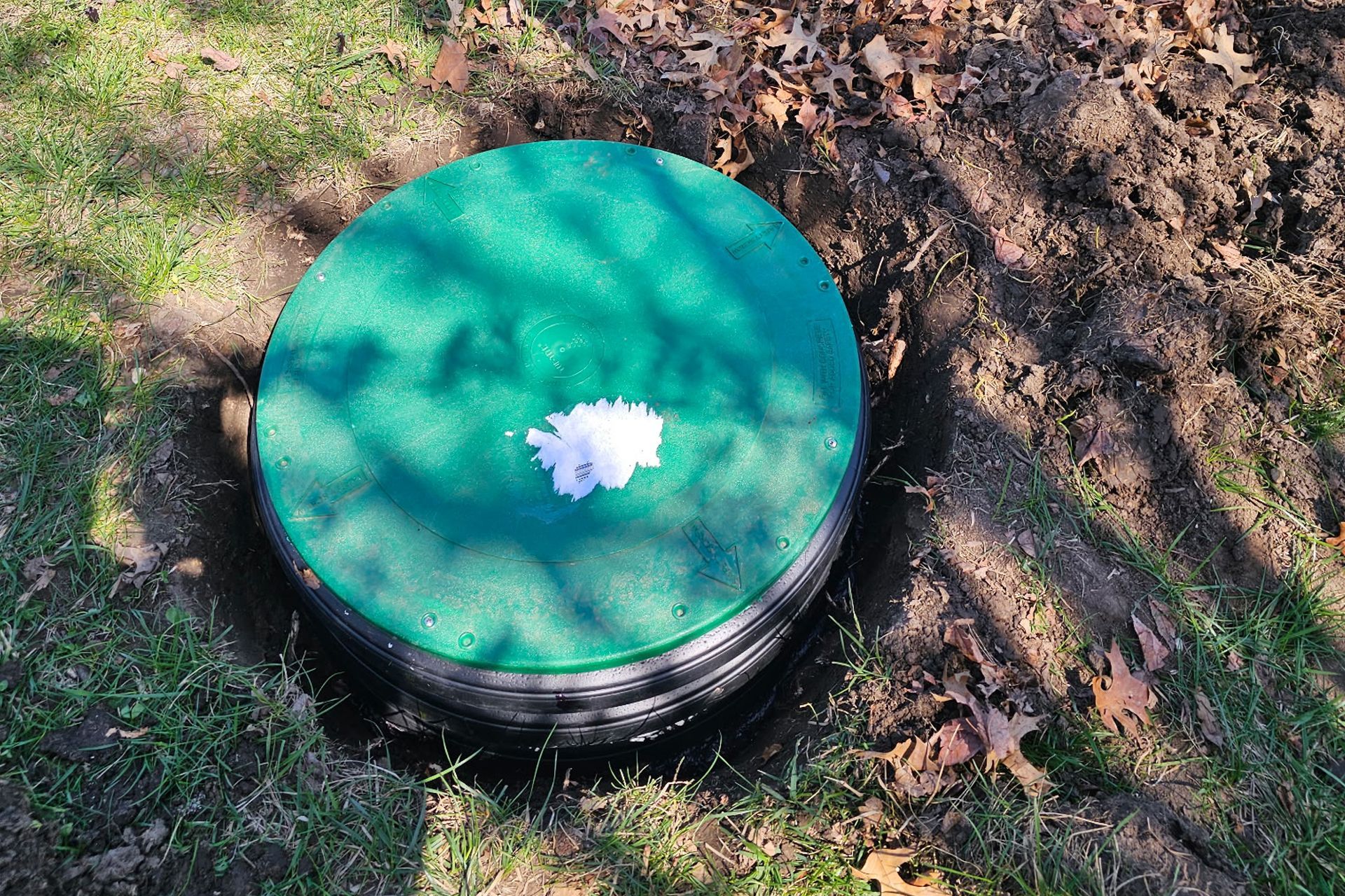 Green septic tank cover partially buried in dirt and grass.
