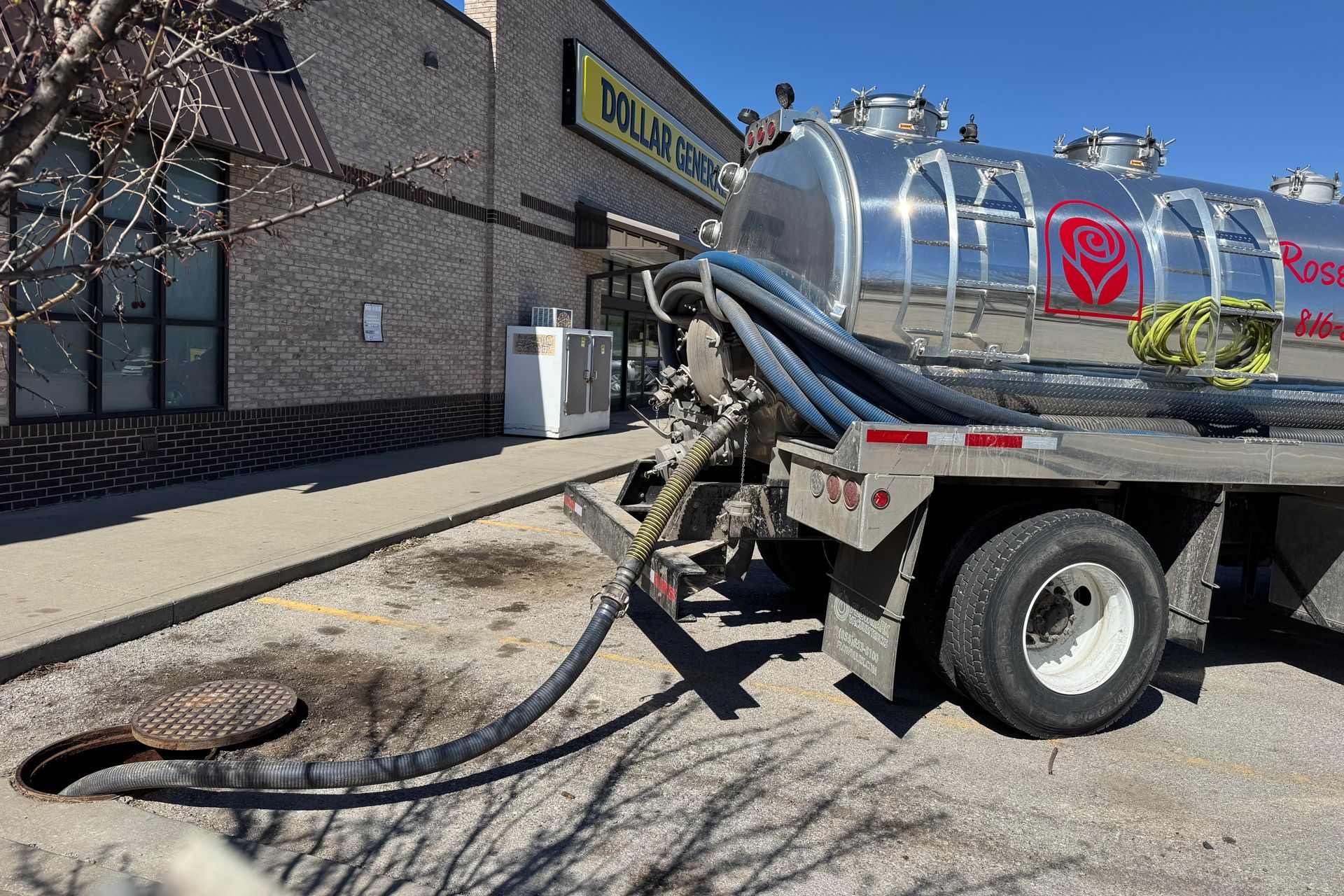 White septic tank truck with an excavator. A worker stands near the truck in a daytime setting.