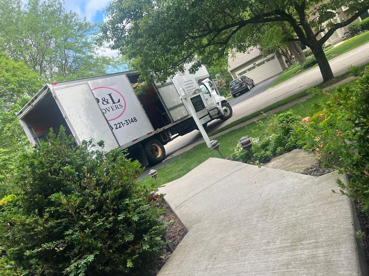 White delivery truck on a tree-lined driveway beside a garden path and bushes