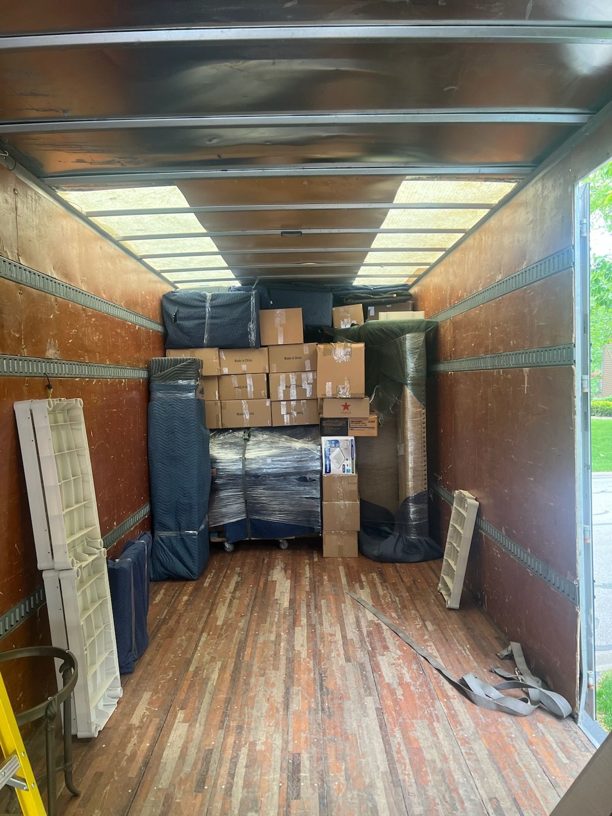 Inside a moving truck, stacked cardboard boxes and wrapped furniture fill the cargo area.