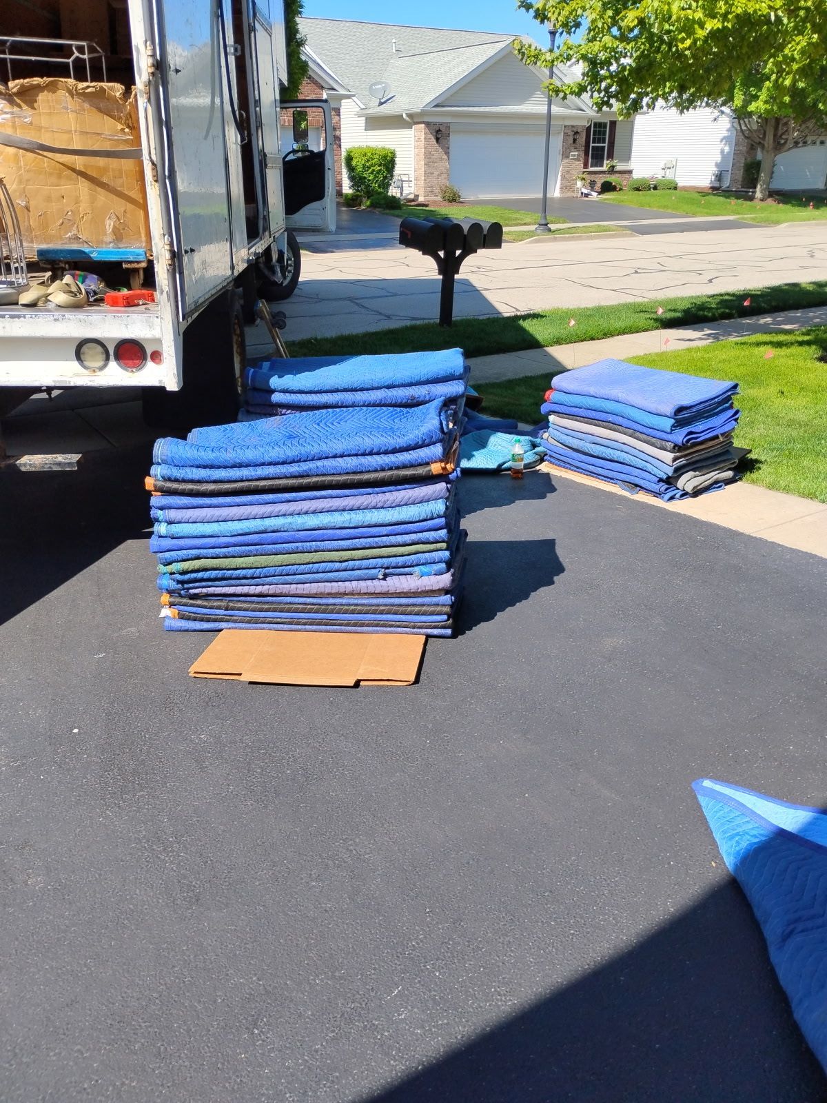 Stacks of blue moving blankets and cardboard on a driveway beside a truck in a suburban neighborhood