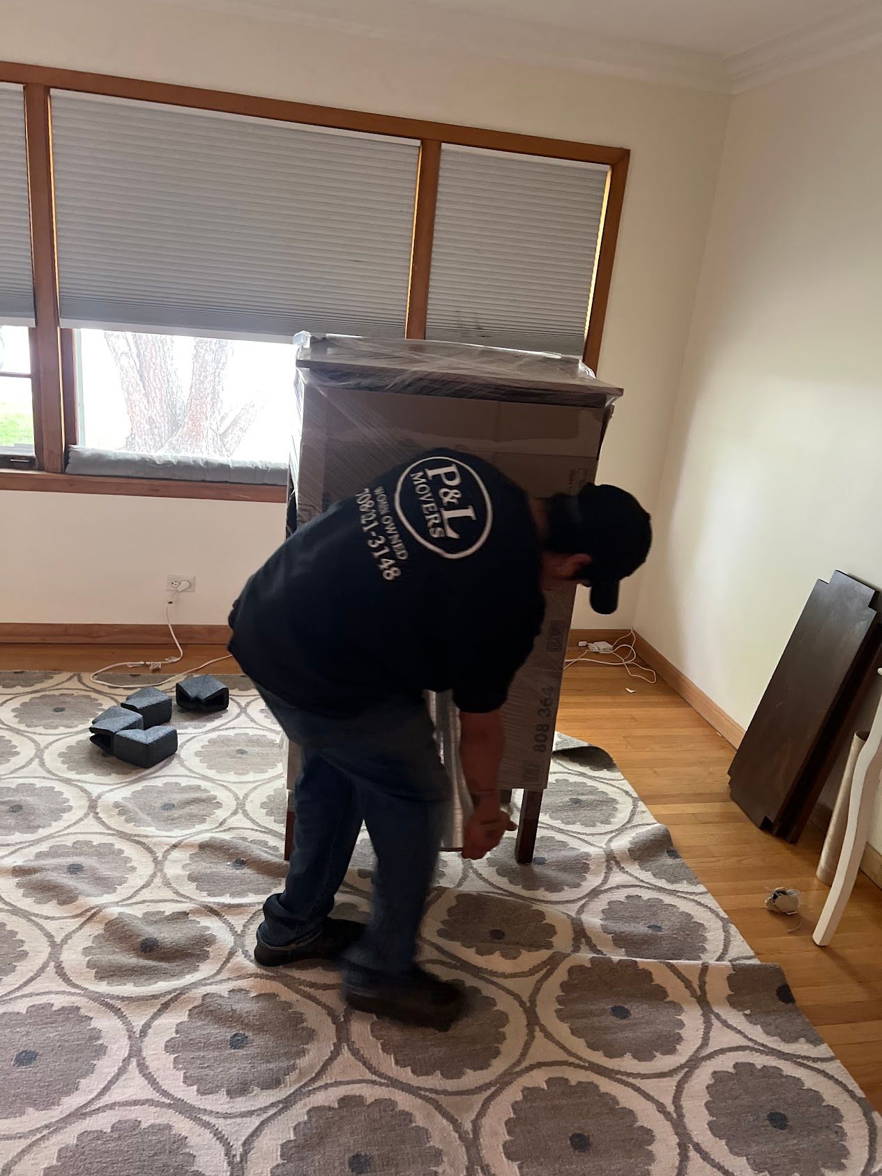 Person assembling a wooden chair in a carpeted room with a window and blinds