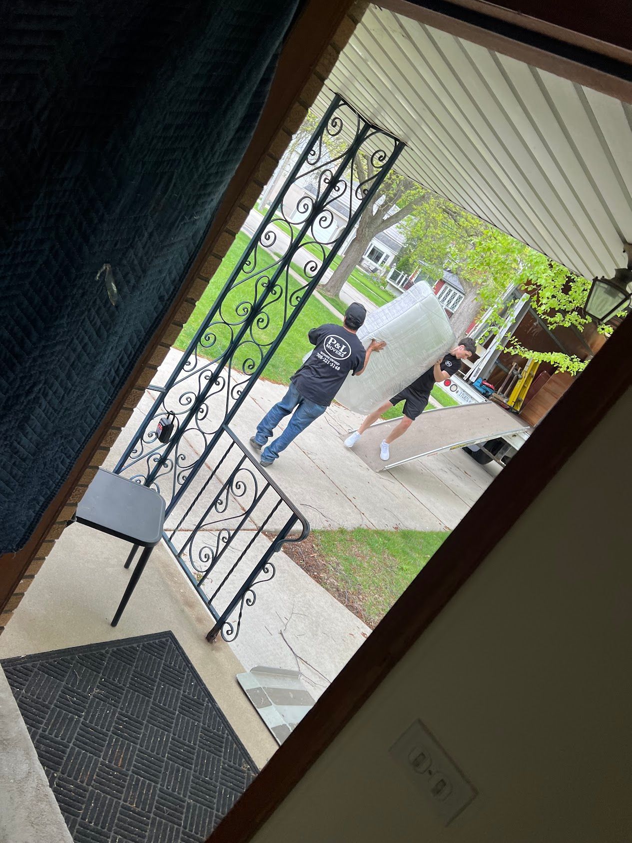 Person carrying a large white board up a sidewalk by a house entrance, seen from a tilted doorway view.