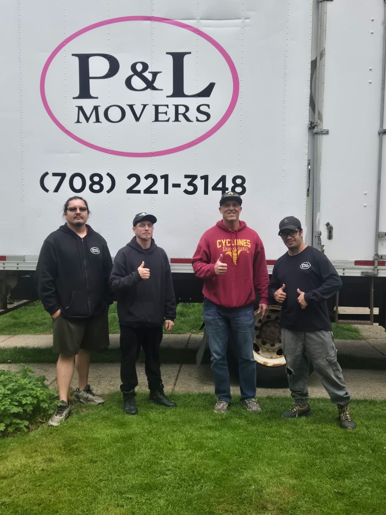 Four workers stand in front of a P&L Movers truck with the phone number.
