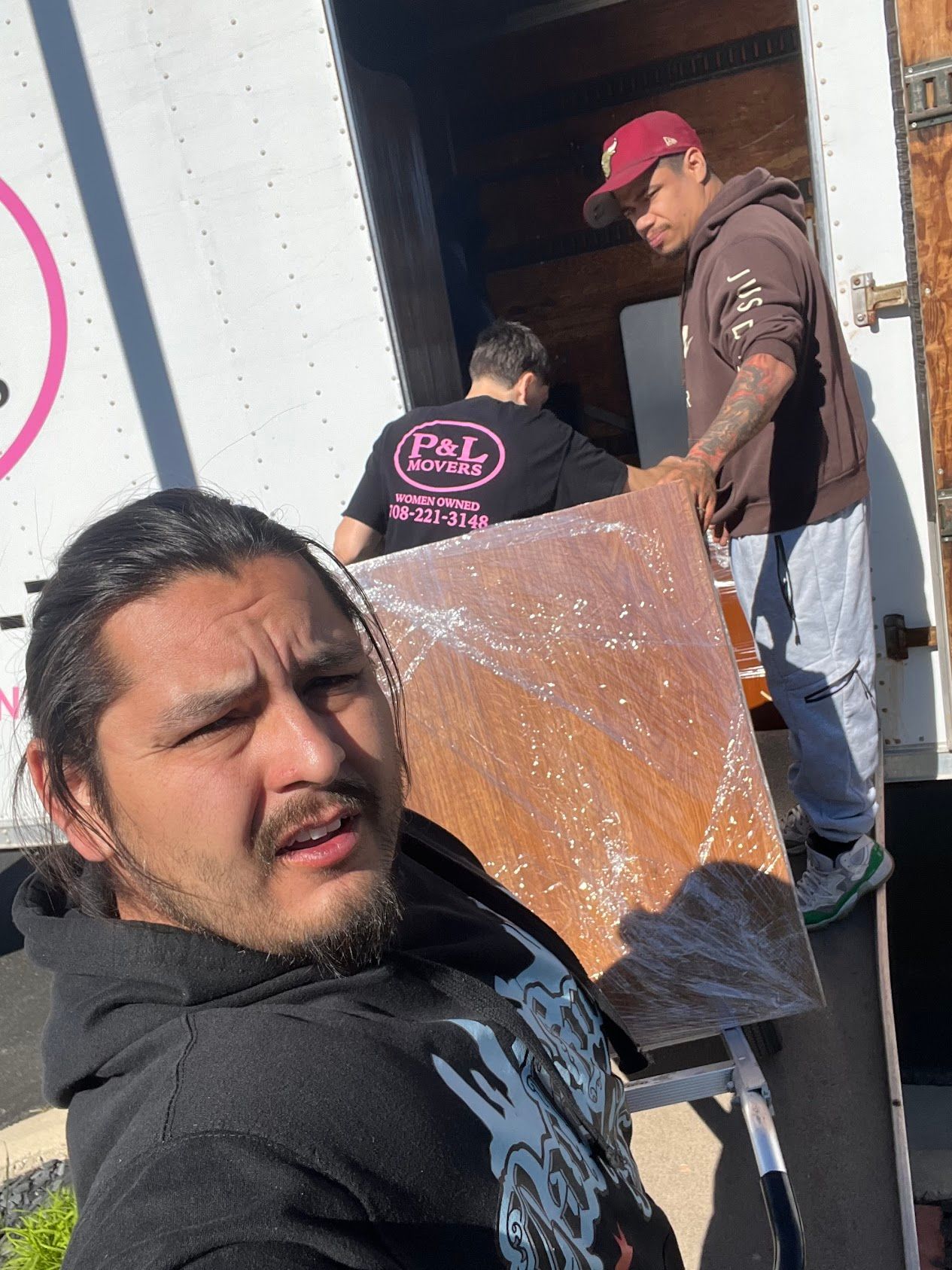 Two men handling a large cardboard sheet outside a building, one looking at the camera.