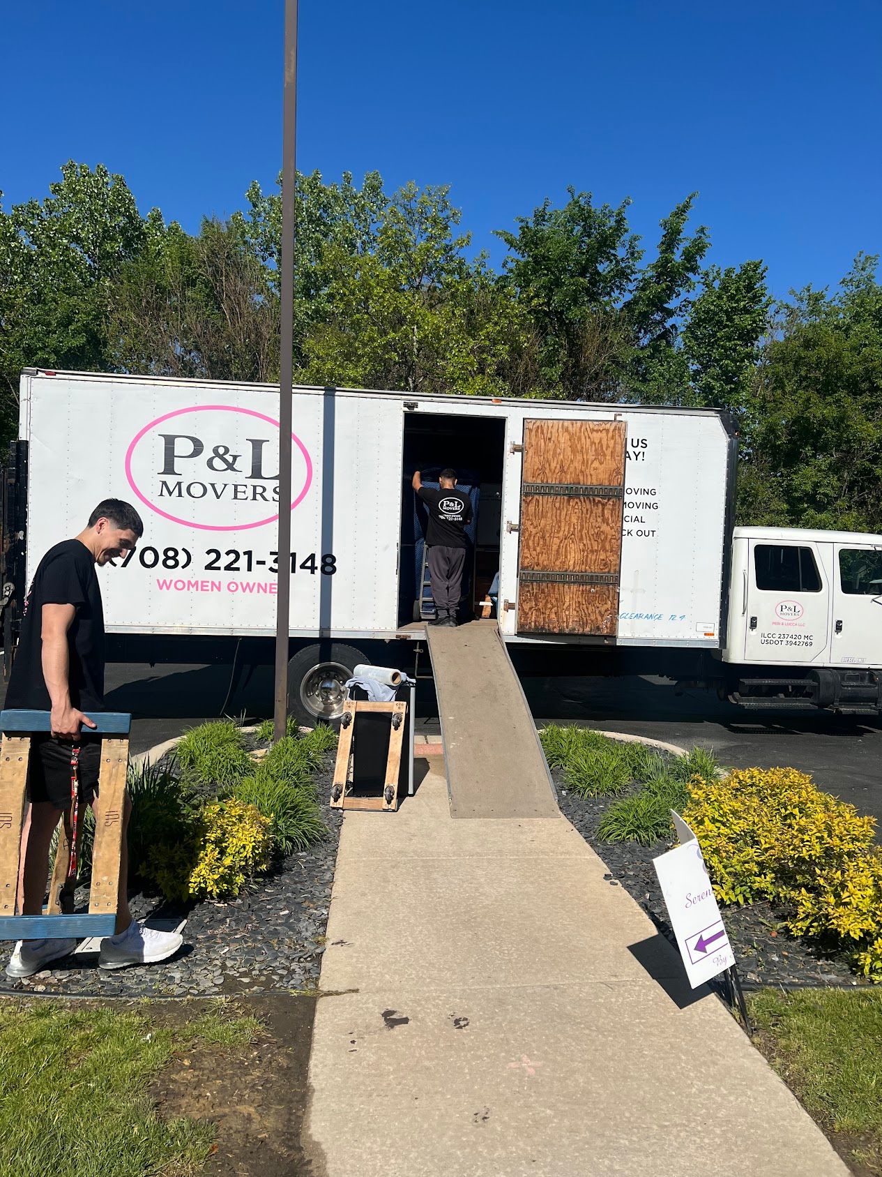 Movers loading boxes into a white truck up a ramp outside a building on a sunny day