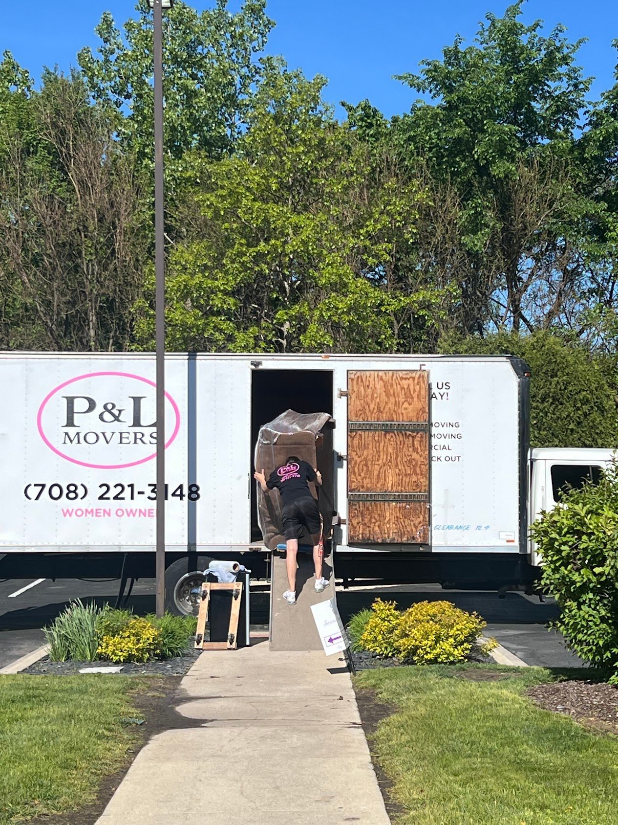 Person loading a white moving truck at a storefront on a sunny day