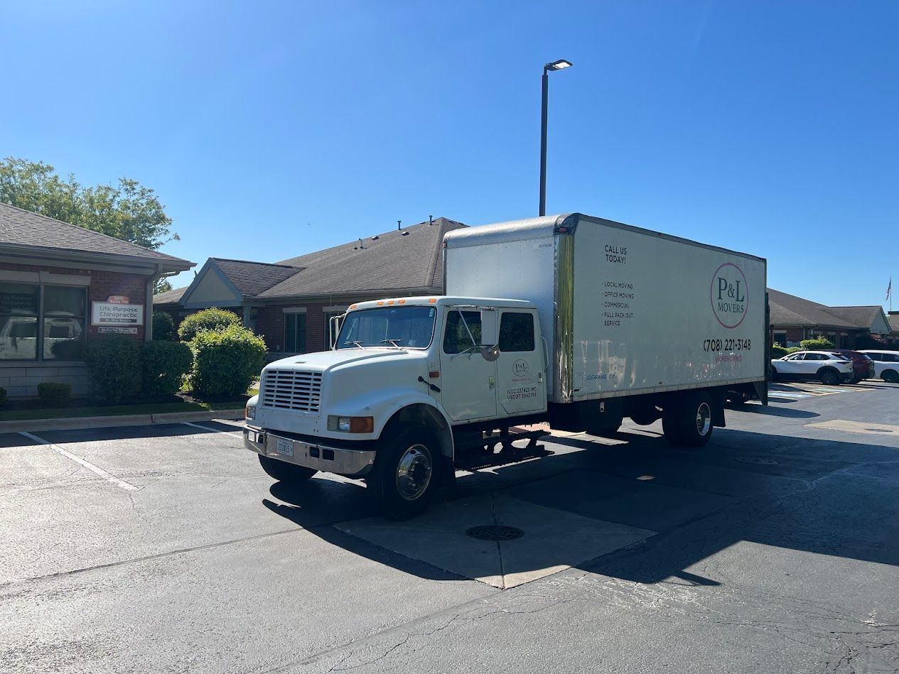 White box truck parked on a sunny residential street beside single-story houses.