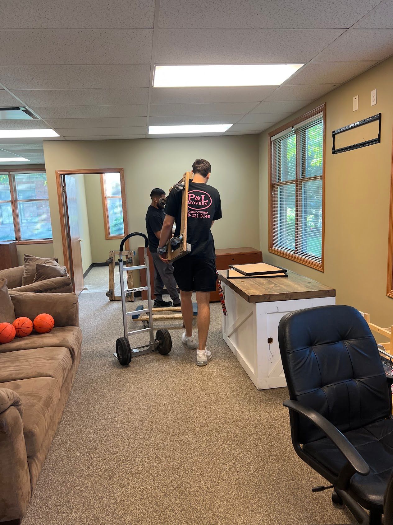 People moving furniture in a living room with couch, orange balls, and white cabinets