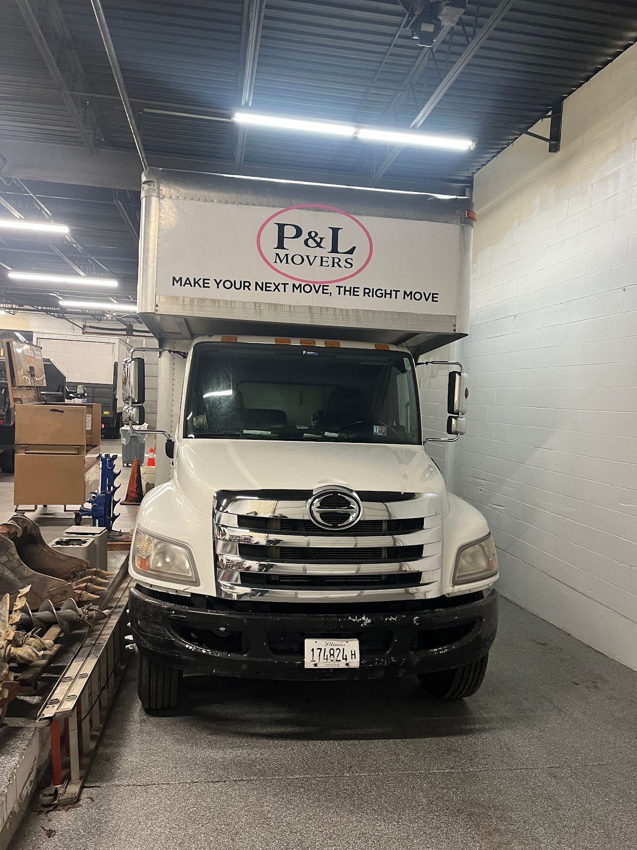 White delivery truck parked inside a narrow warehouse bay under bright lights
