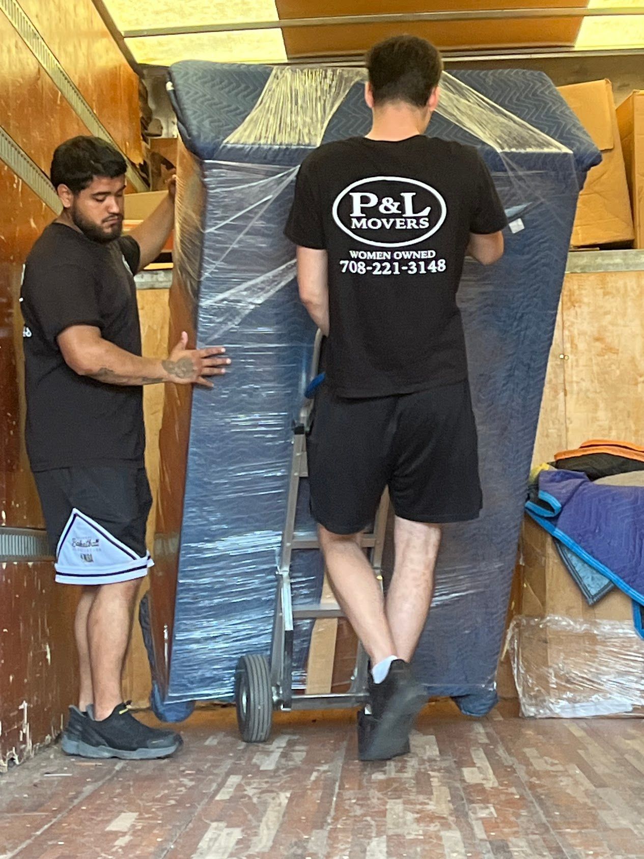 Two movers carrying a wrapped refrigerator through a doorway with a hand truck