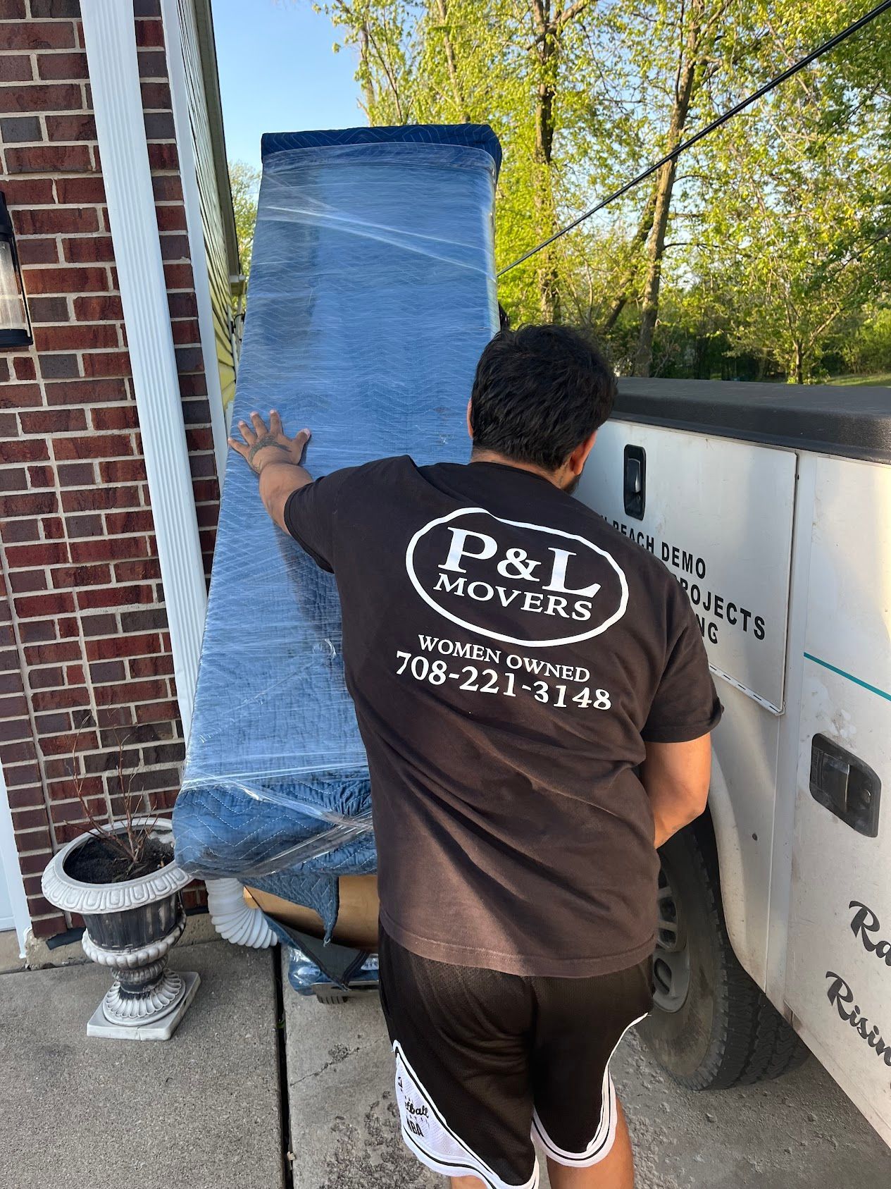 Worker applying blue roofing underlayment beside a brick house and trailer.