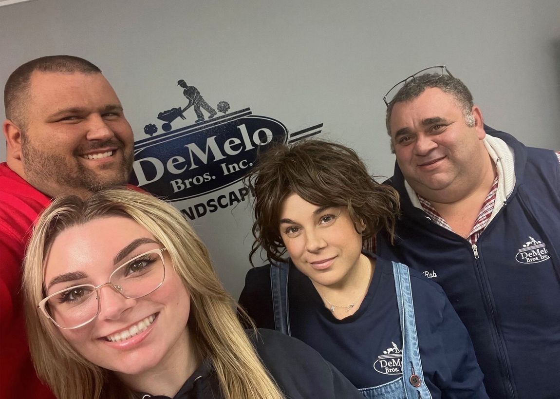 A group of people are posing for a picture in front of a demelo bros. inc. sign.