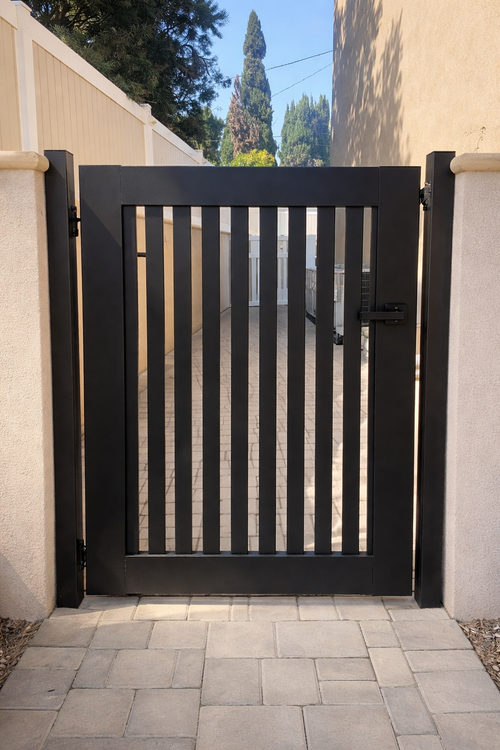 Black slatted metal gate between beige walls with a paved walkway leading to it