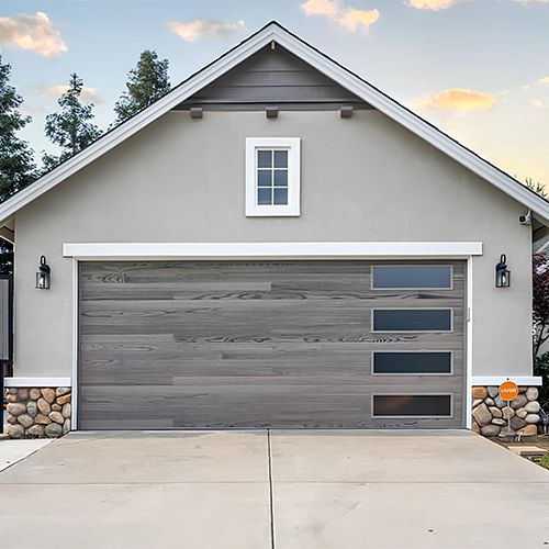 Gray garage with a wood-look door, horizontal glass panels, and stone accents.