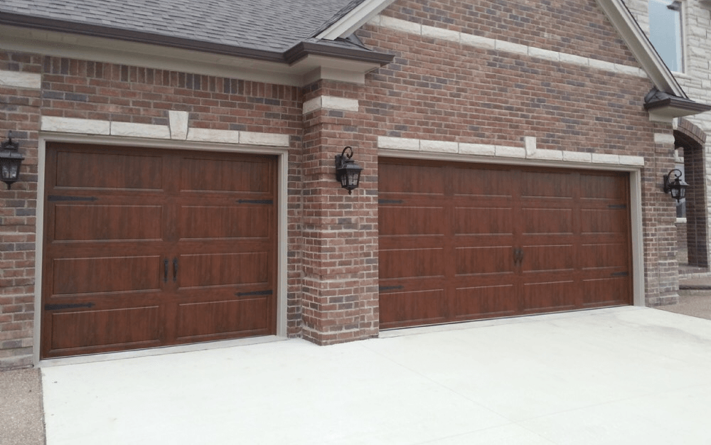 Two brown garage doors on a brick house with concrete driveway.