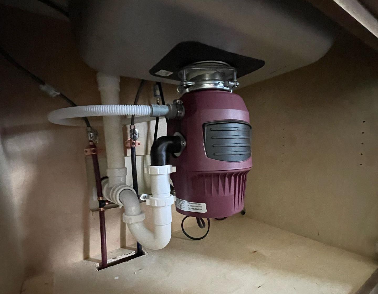 Garbage disposal unit installed under a kitchen sink with connected plumbing.