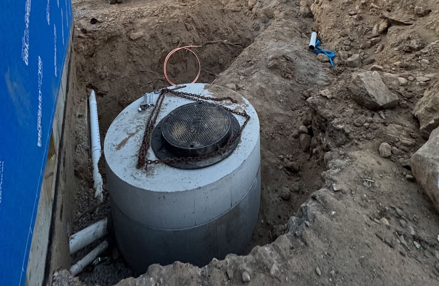 Concrete septic tank in an excavated trench, next to a blue wall.