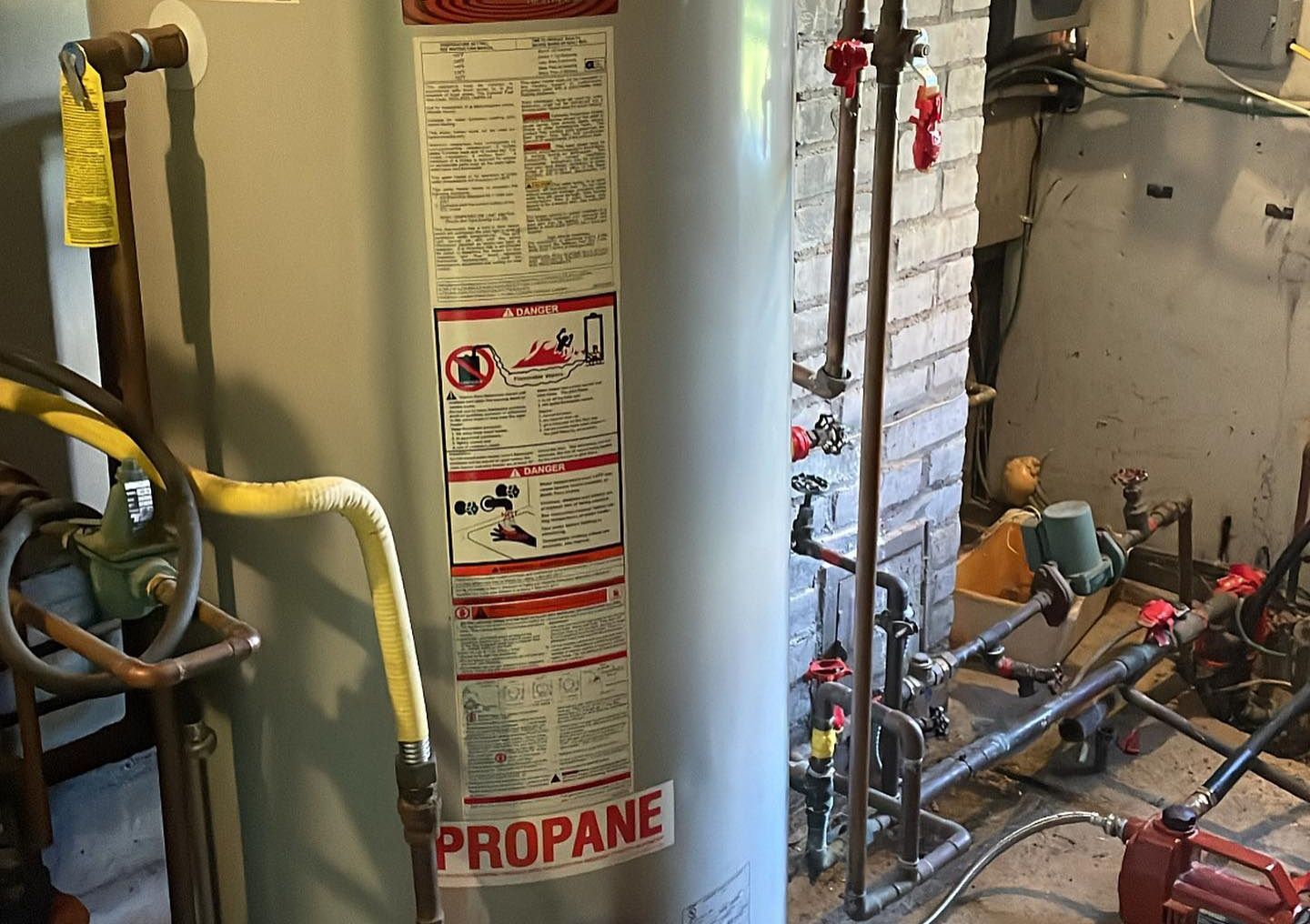 A propane water heater in a basement with attached pipes and safety labels.