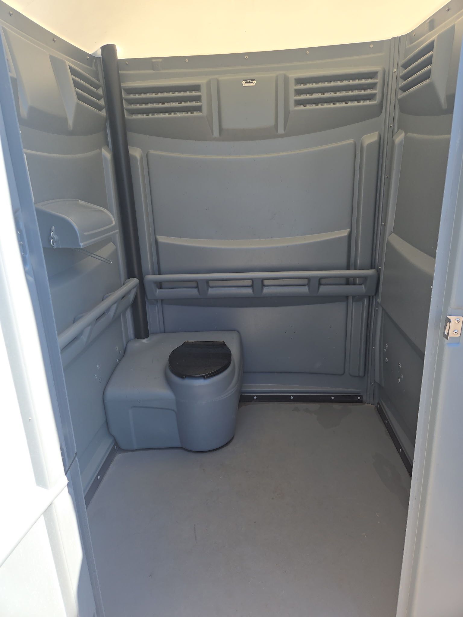 Interior of a gray portable toilet. Features include a toilet seat, hand sanitizer dispenser, and ventilation.