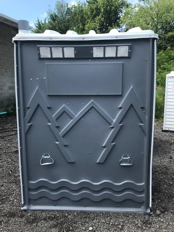 Gray portable toilet with mountain and wave design, in outdoor setting.