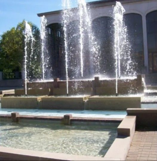Multiple fountains shoot vertical streams of water into the air in front of a modern building with large glass windows.