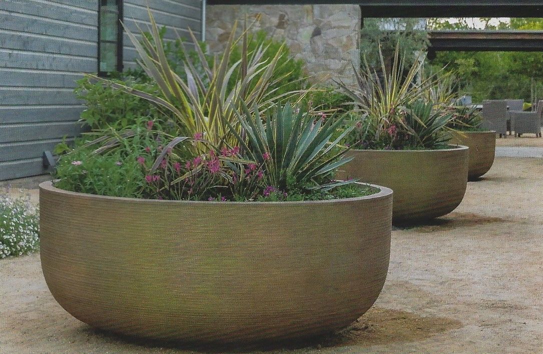 Large, textured, bowl-shaped planters with ornamental grasses and succulents on a gravel patio by a modern building.