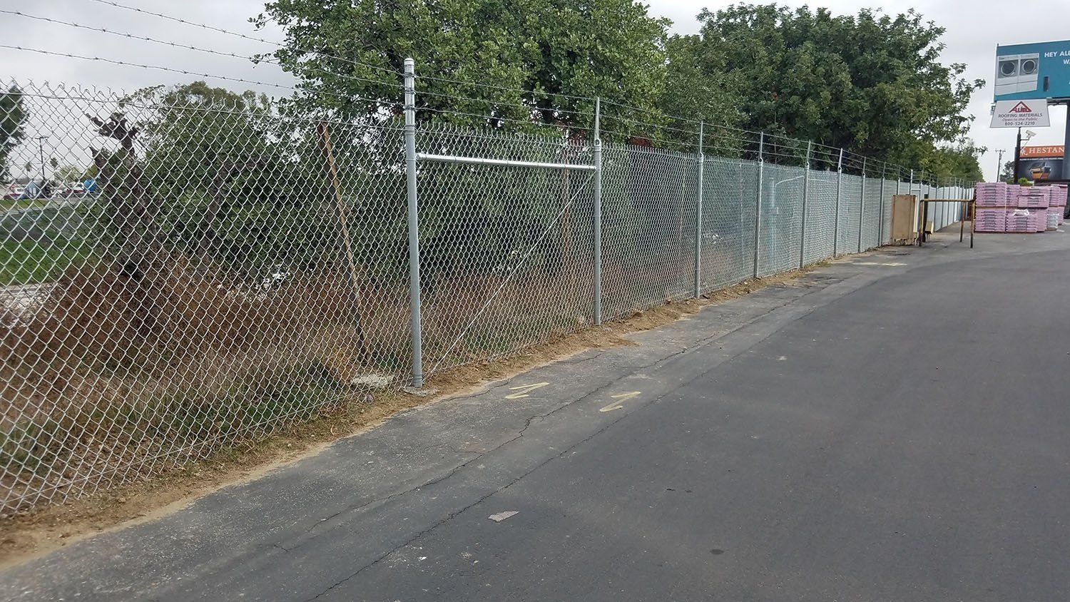 Chain link fence alongside a road, trees in the background.