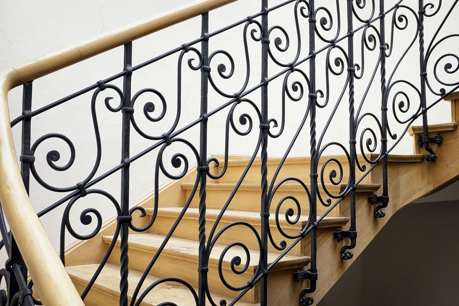 Staircase with wooden steps and ornate black iron railing, topped with a light-colored wooden handrail.