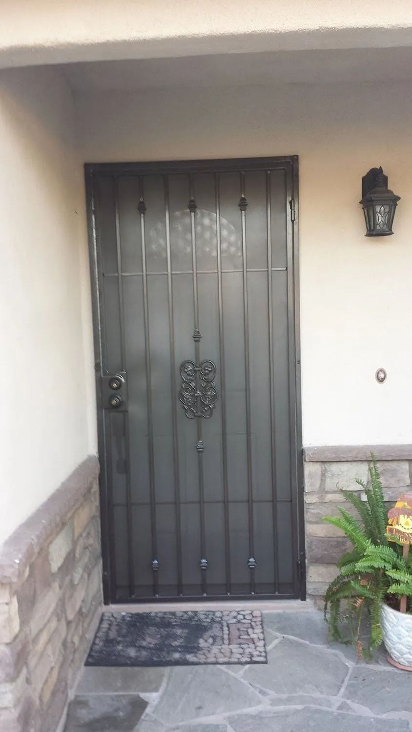 Black security door with decorative center detail; on a stone and beige exterior.