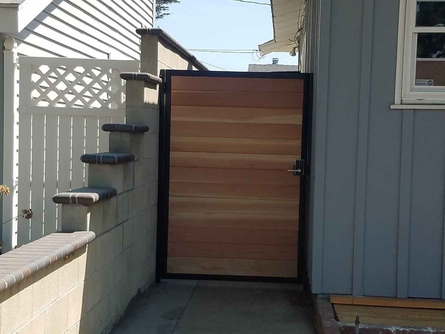 Wooden gate with black frame, next to steps and blue house.