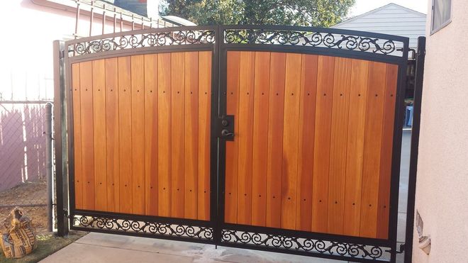 Wooden double gate with black metal frame and ornate scrollwork.