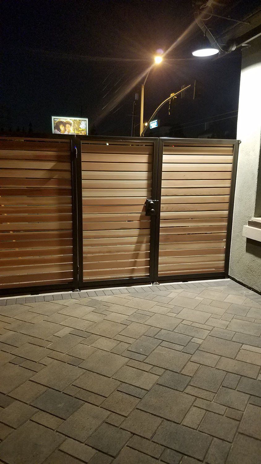 Wooden gate, brick patio, lit by a street lamp at night.