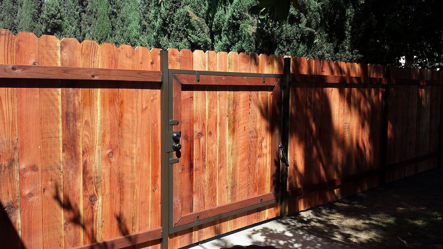 Wooden fence with a gate, stained reddish-brown. The gate is closed and has black metal framing.