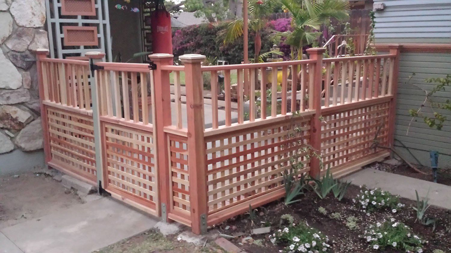 Wooden lattice fence with a gate enclosing a front yard garden.