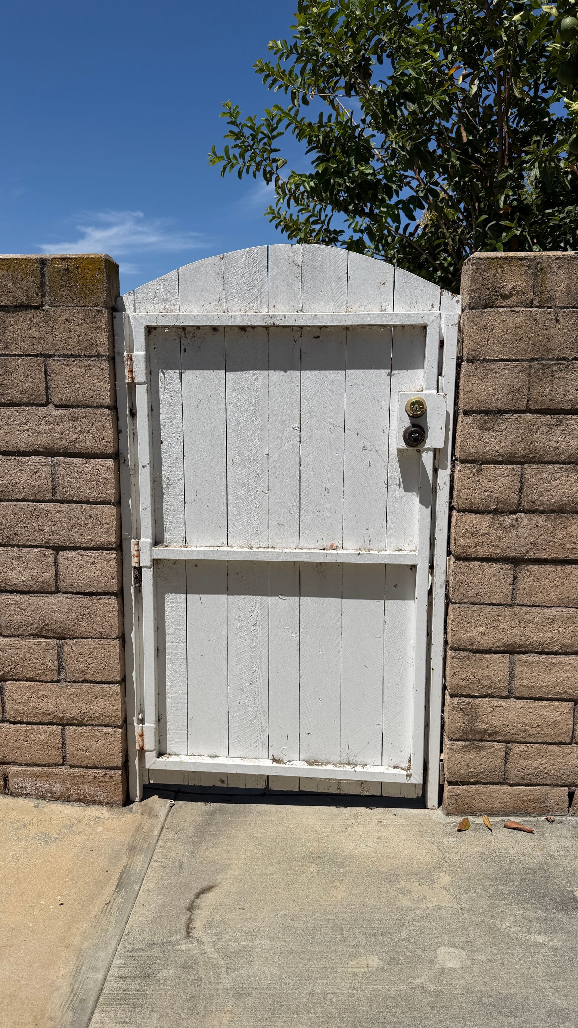 White wooden gate between stone pillars beside a concrete driveway under a blue sky.