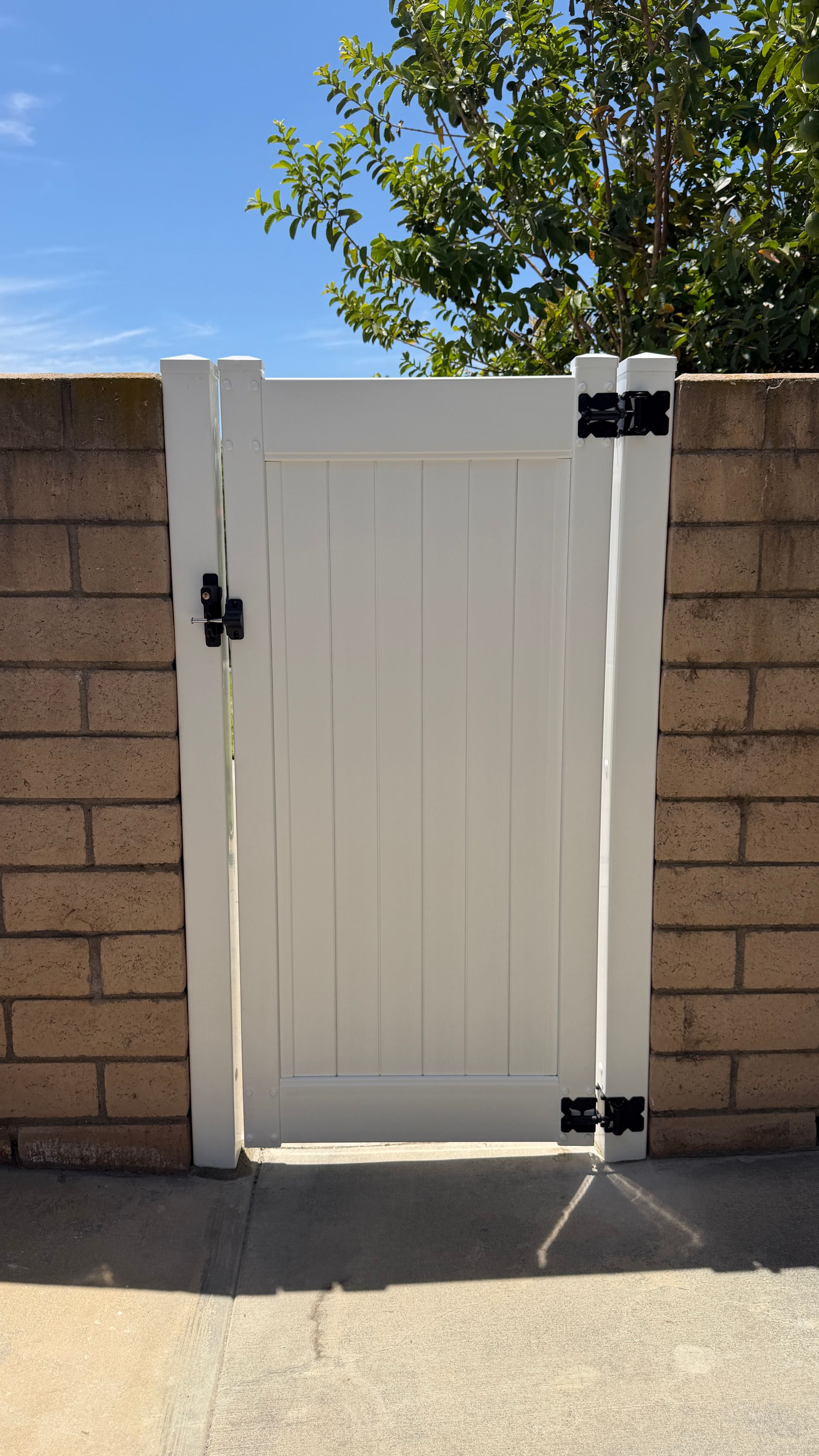 White wooden gate between tan brick walls in bright sunlight, with black hinges and latch.