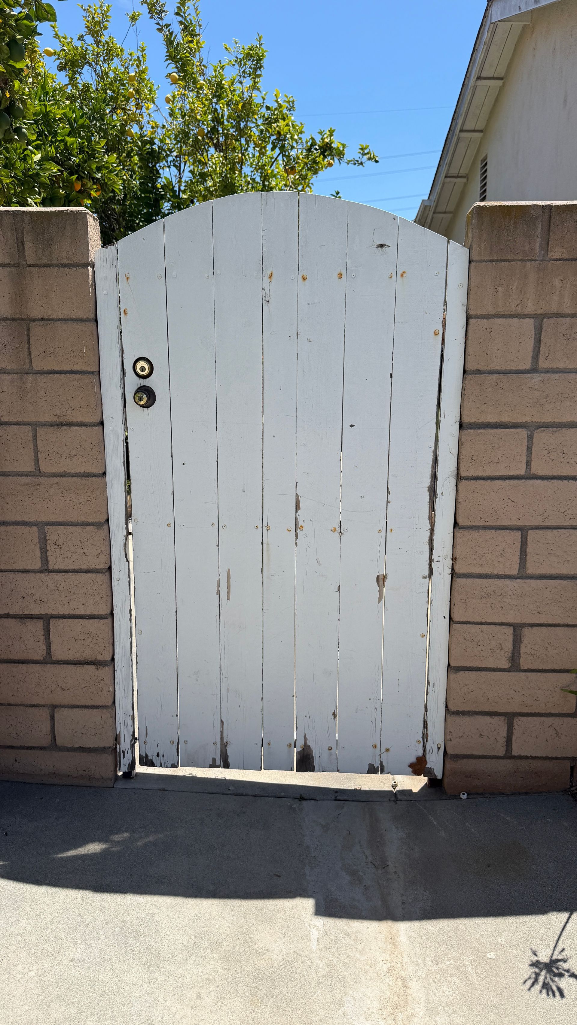 White wooden gate between tan brick walls, with a round handle, in bright sunlight.