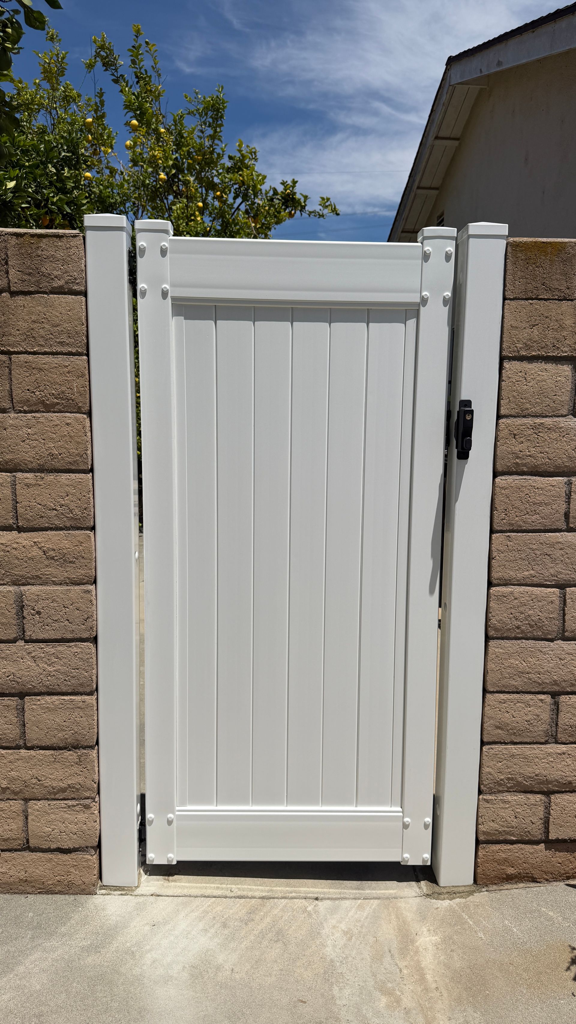 White pedestrian gate in a tan brick wall under a sunny sky