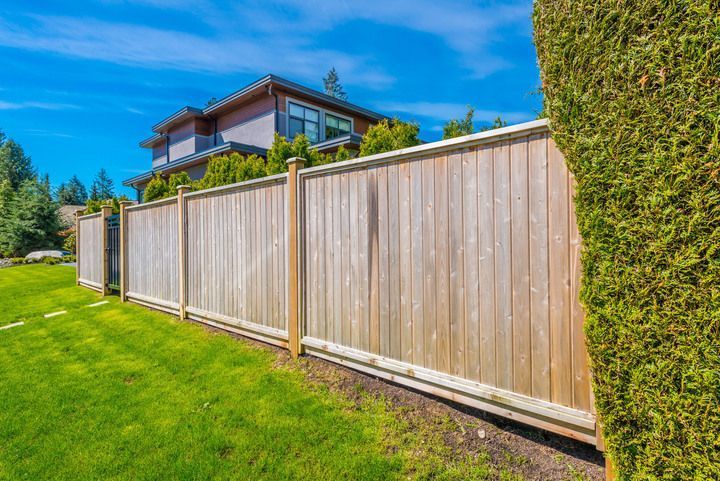 Wooden fence in a backyard with green grass and a house in the background on a sunny day.