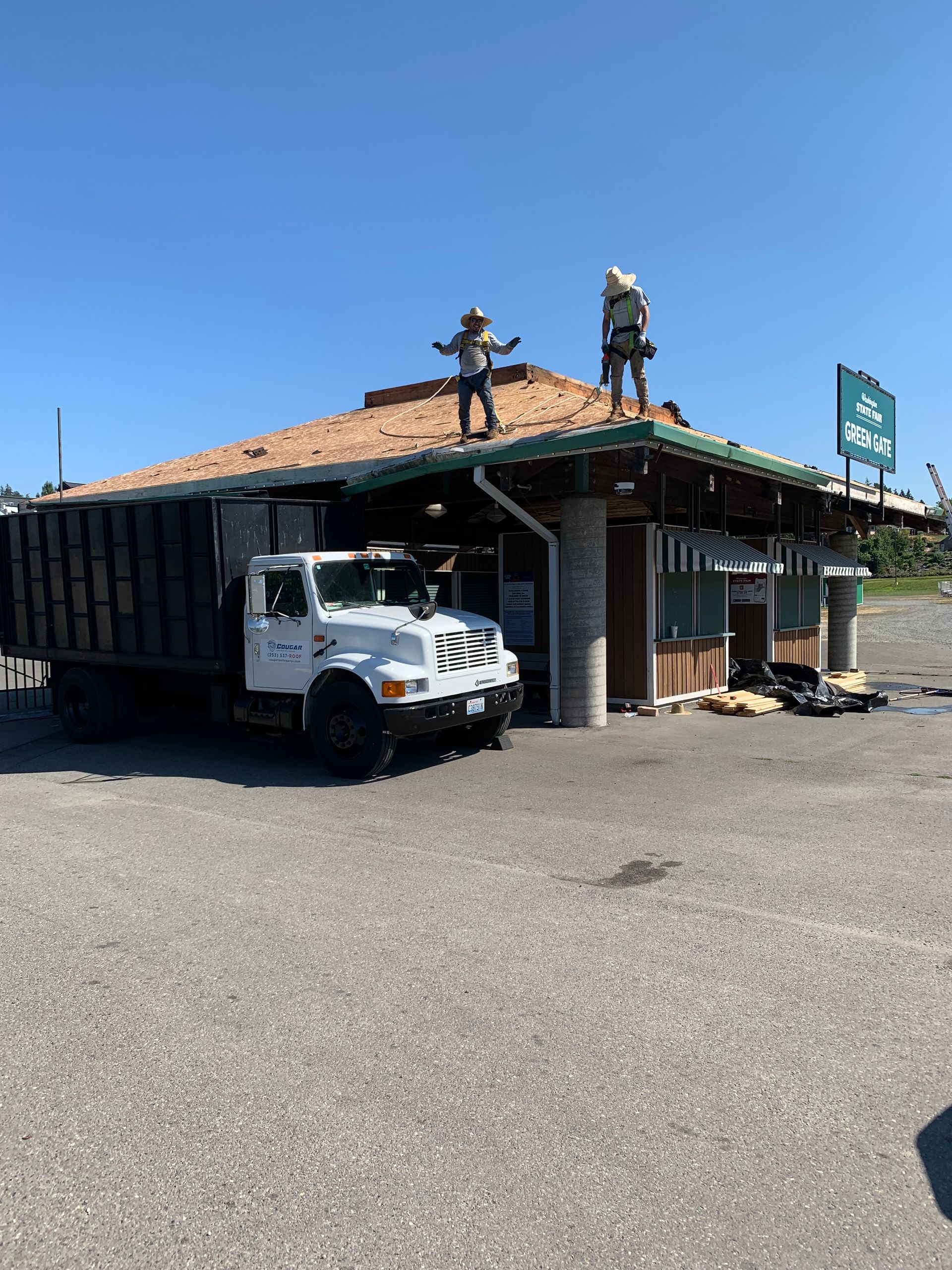 A truck is parked in front of a building with workers on the roof.