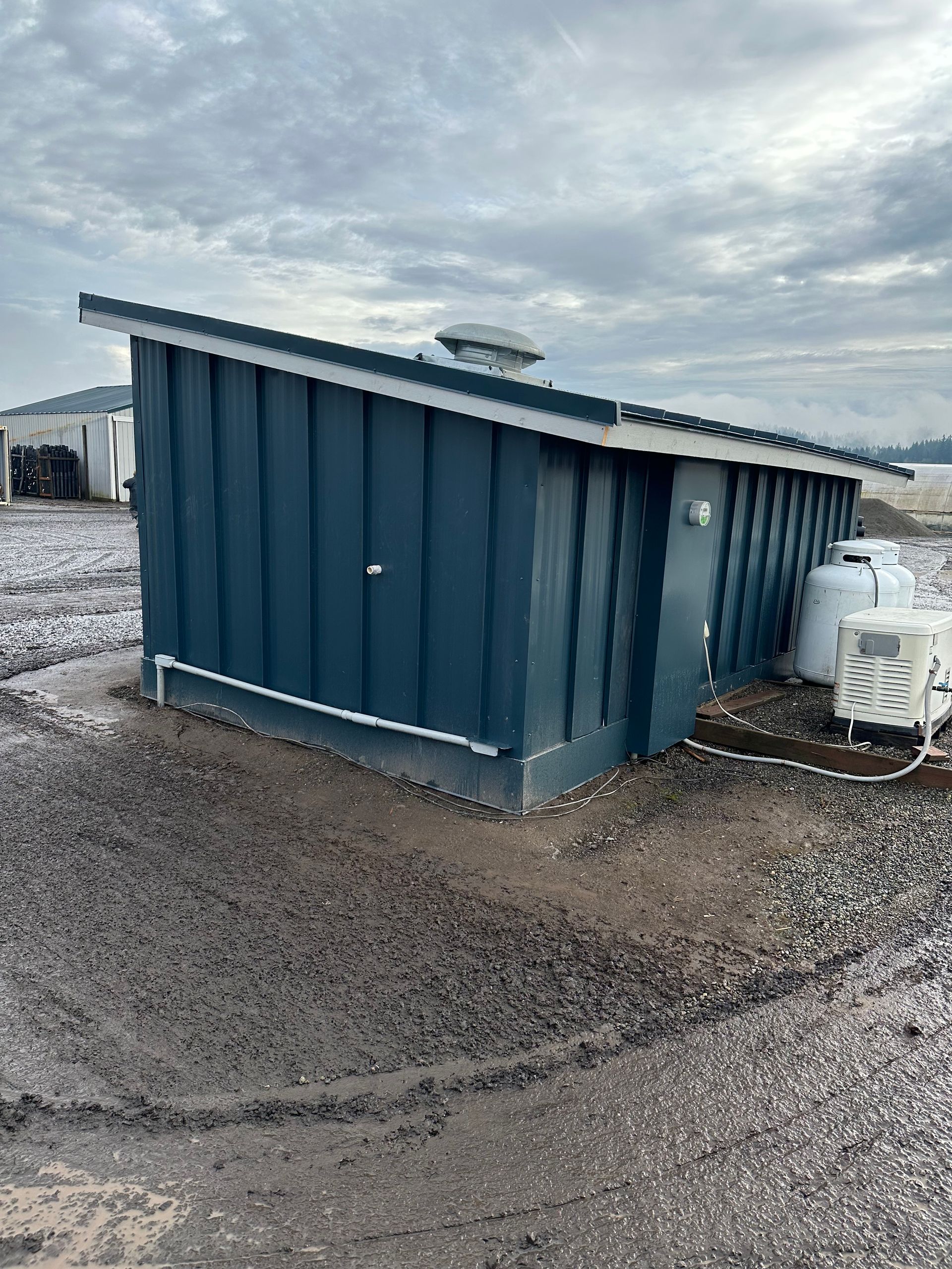A small blue building with a roof is sitting in the middle of a dirt field.