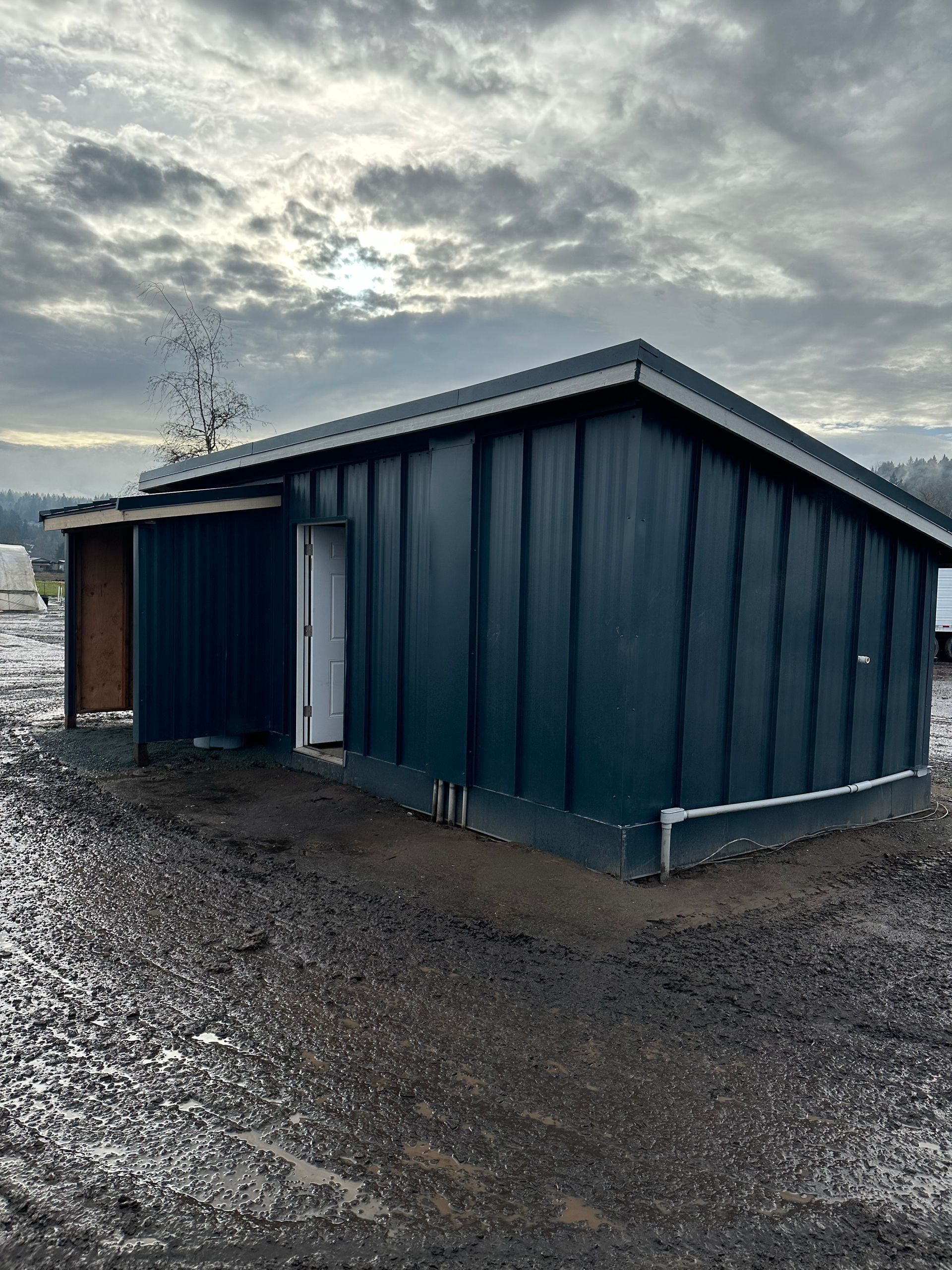 A blue shed is sitting in the middle of a dirt field.