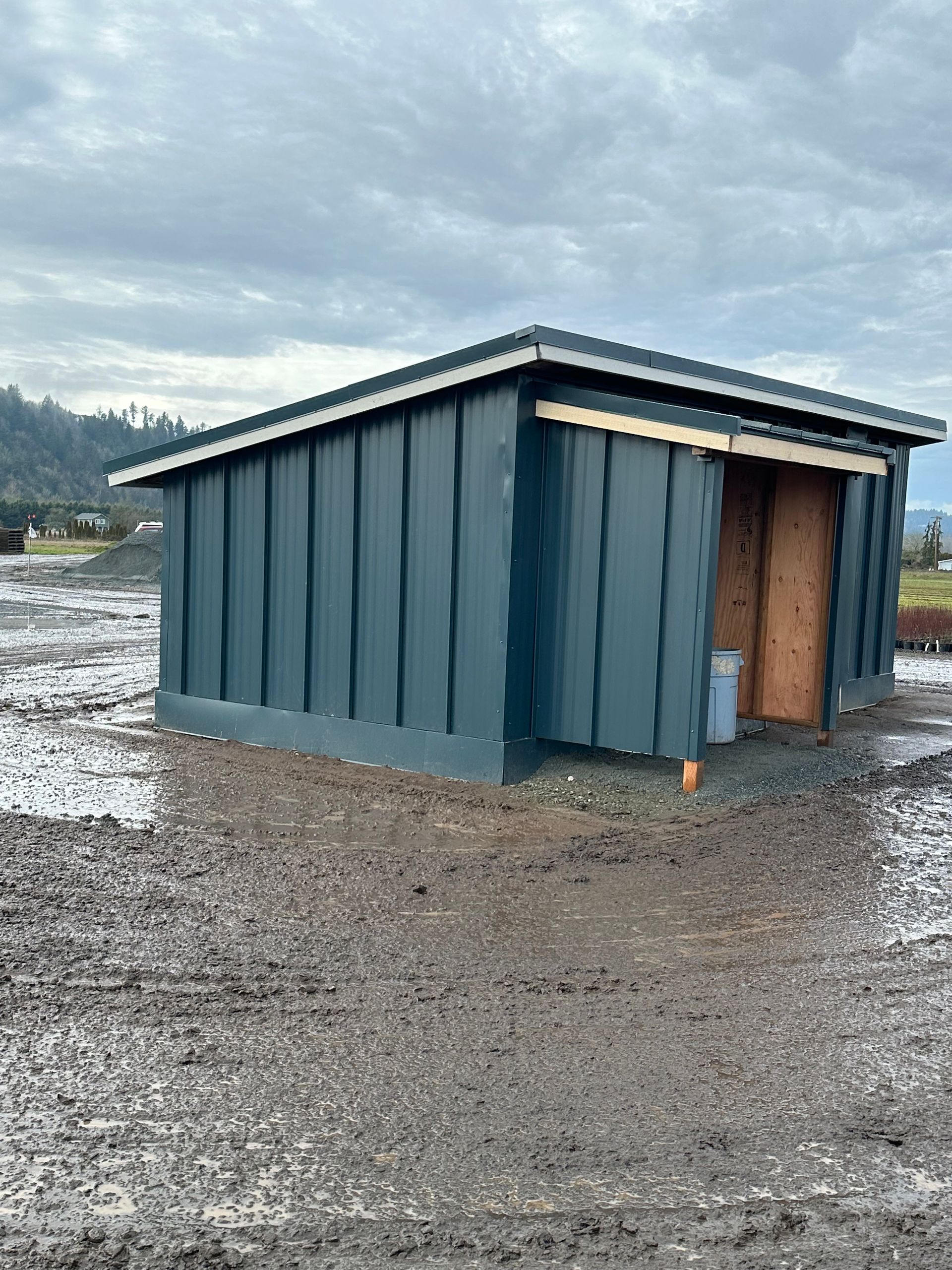 A small shed is sitting in the middle of a dirt field.