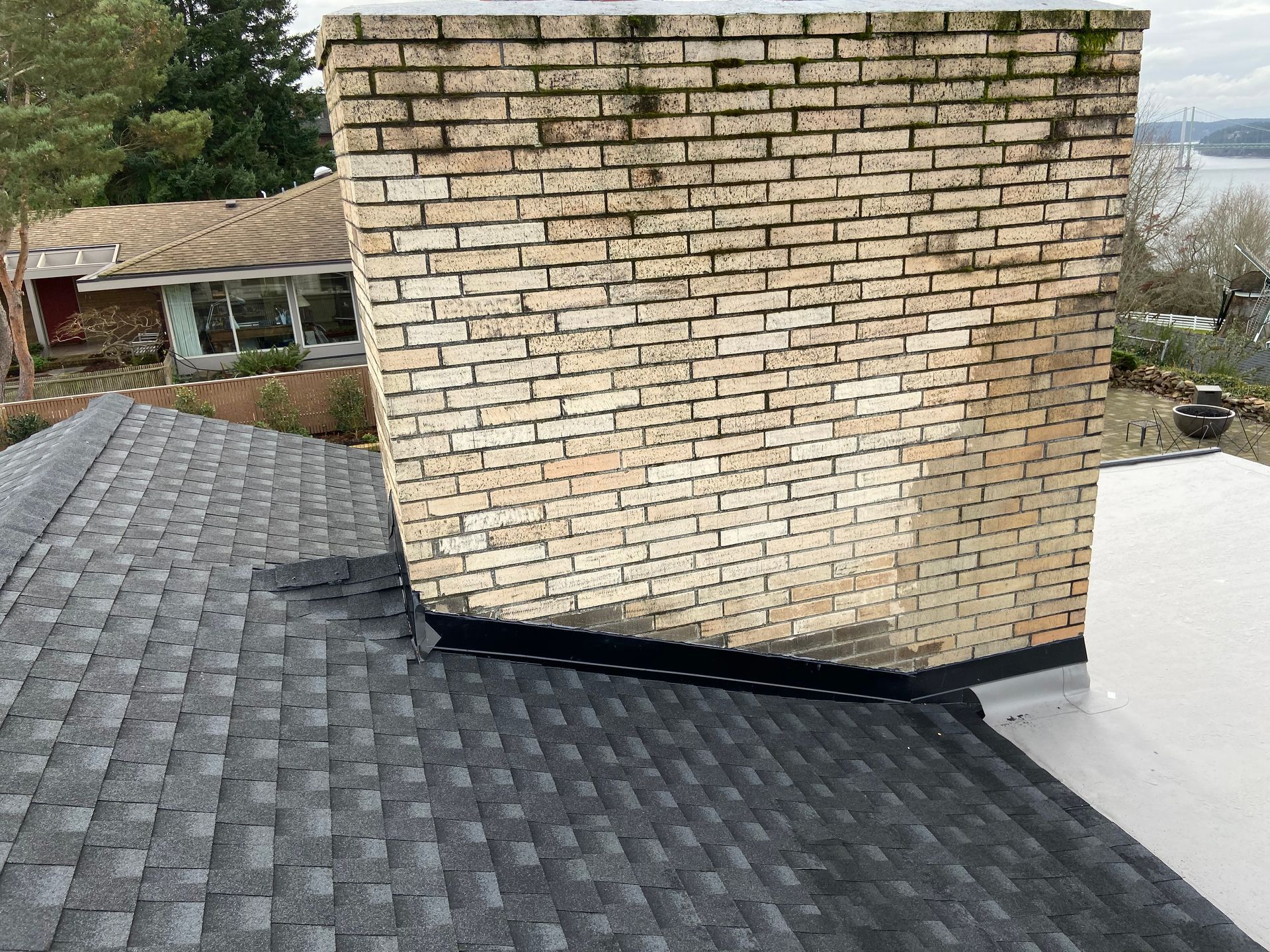A brick chimney is sitting on top of a roof next to a house.