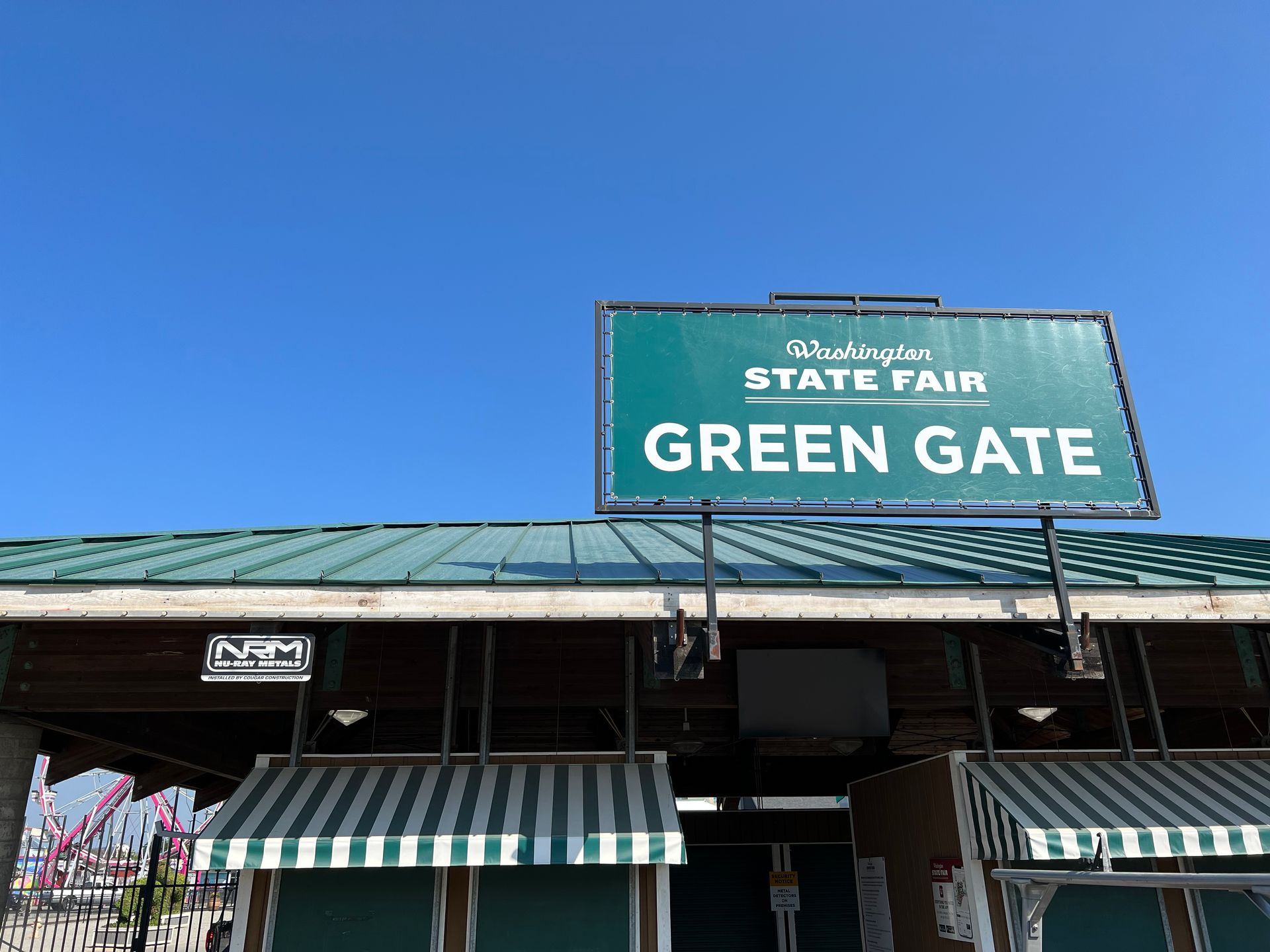 A green gate sign is hanging from the roof of a building.